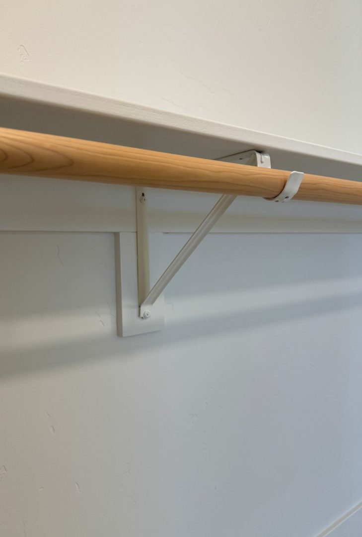 Knape & Vogt heavy-duty shelf and closet rod bracket in white, installed to support a wooden shelf and closet rod, providing a sturdy solution for organizing clothing and accessories in closets or storage areas.