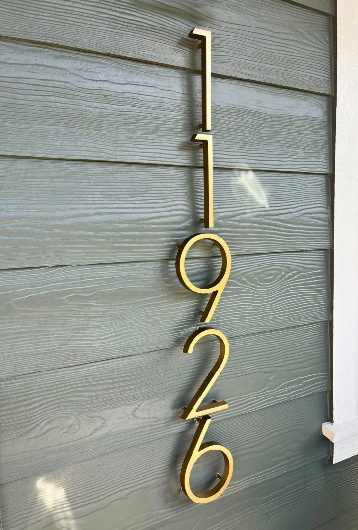 Satin brass Emtek modern house numbers in a sleek satin brass finish, mounted on a contemporary exterior wall, providing clear visibility and a sophisticated look to enhance curb appeal.