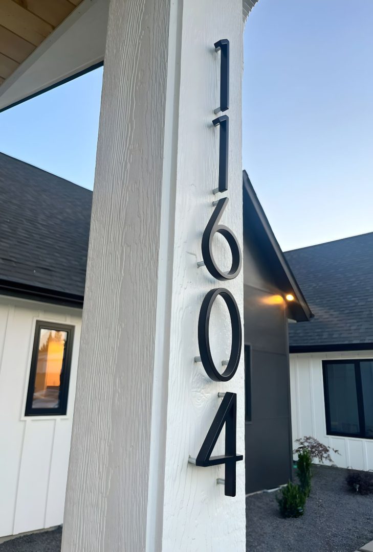 7" Flat Black Emtek modern house numbers in a sleek satin brass finish, mounted on a contemporary exterior wall, providing clear visibility and a sophisticated look to enhance curb appeal.