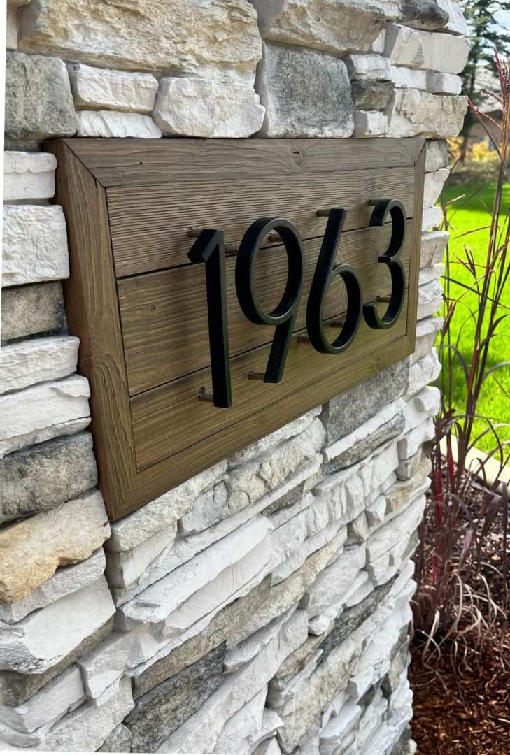 7" Flat Black Emtek modern house numbers in a sleek satin brass finish, mounted on a contemporary exterior wall, providing clear visibility and a sophisticated look to enhance curb appeal.